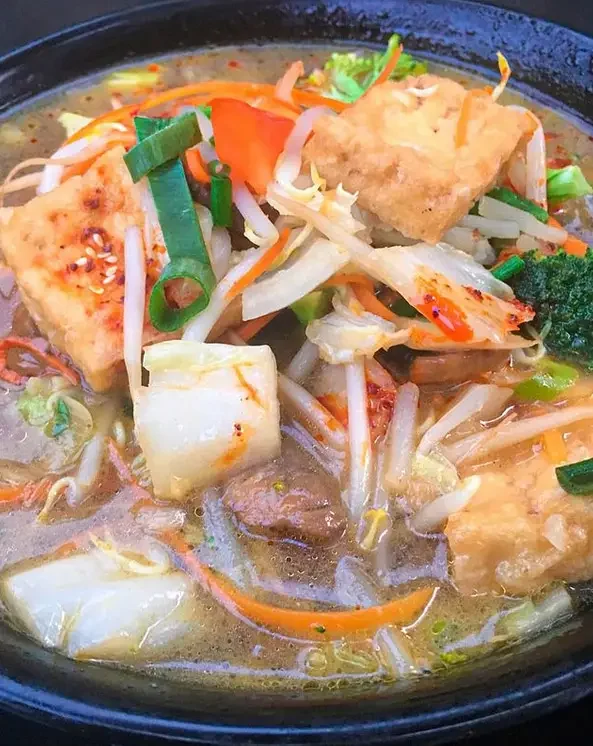Asiatische Suppe mit Fisch und Gemüse in einer dunklen Schale